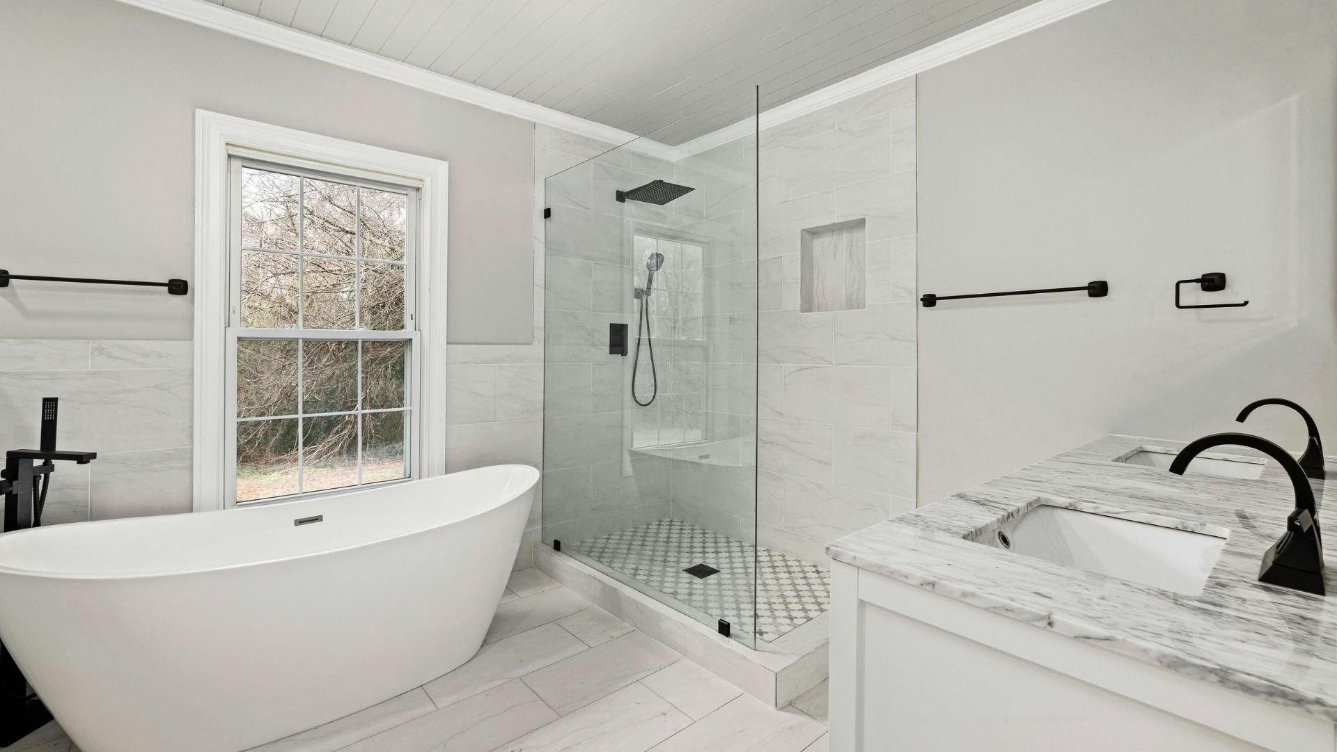 Modern white bathroom with freestanding tub, glass shower enclosure, marble vanity, and large window