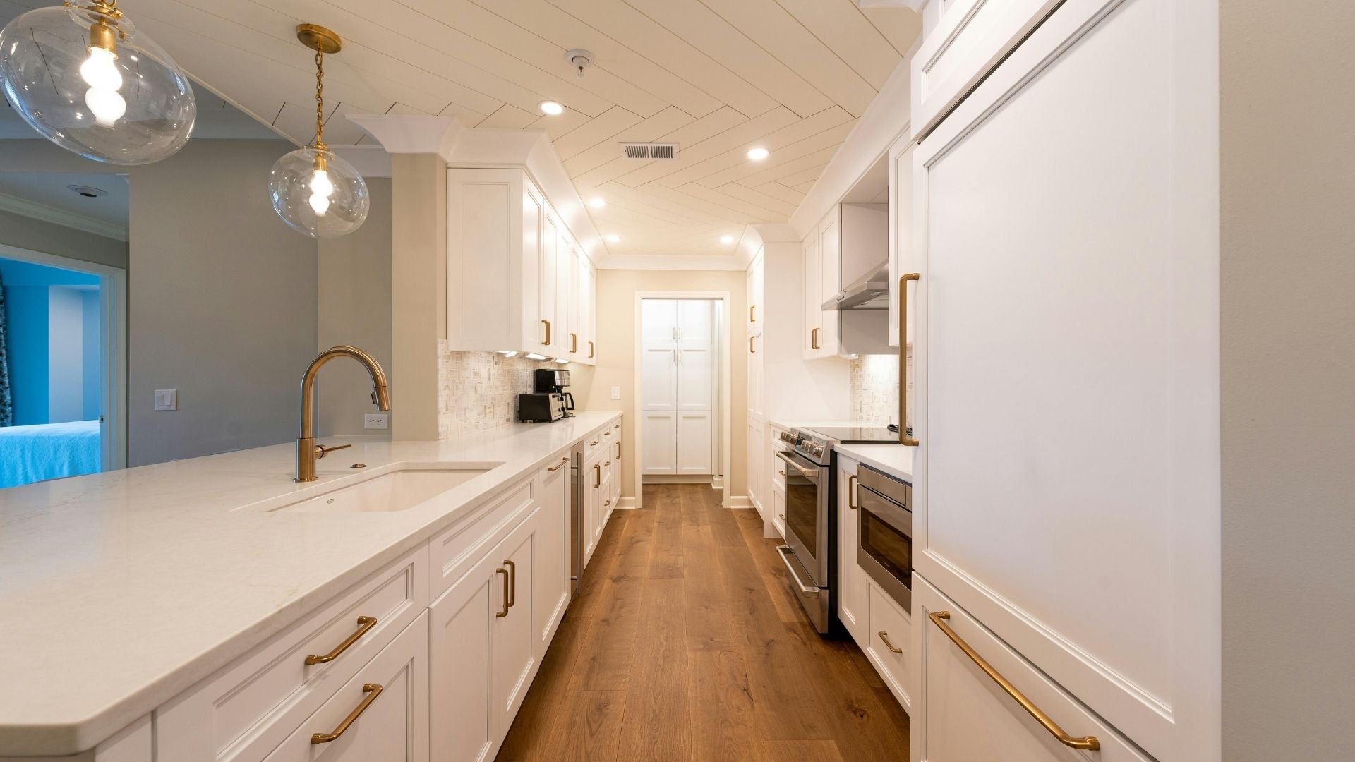 Modern white kitchen with wood floors, white cabinetry, and brass fixtures.