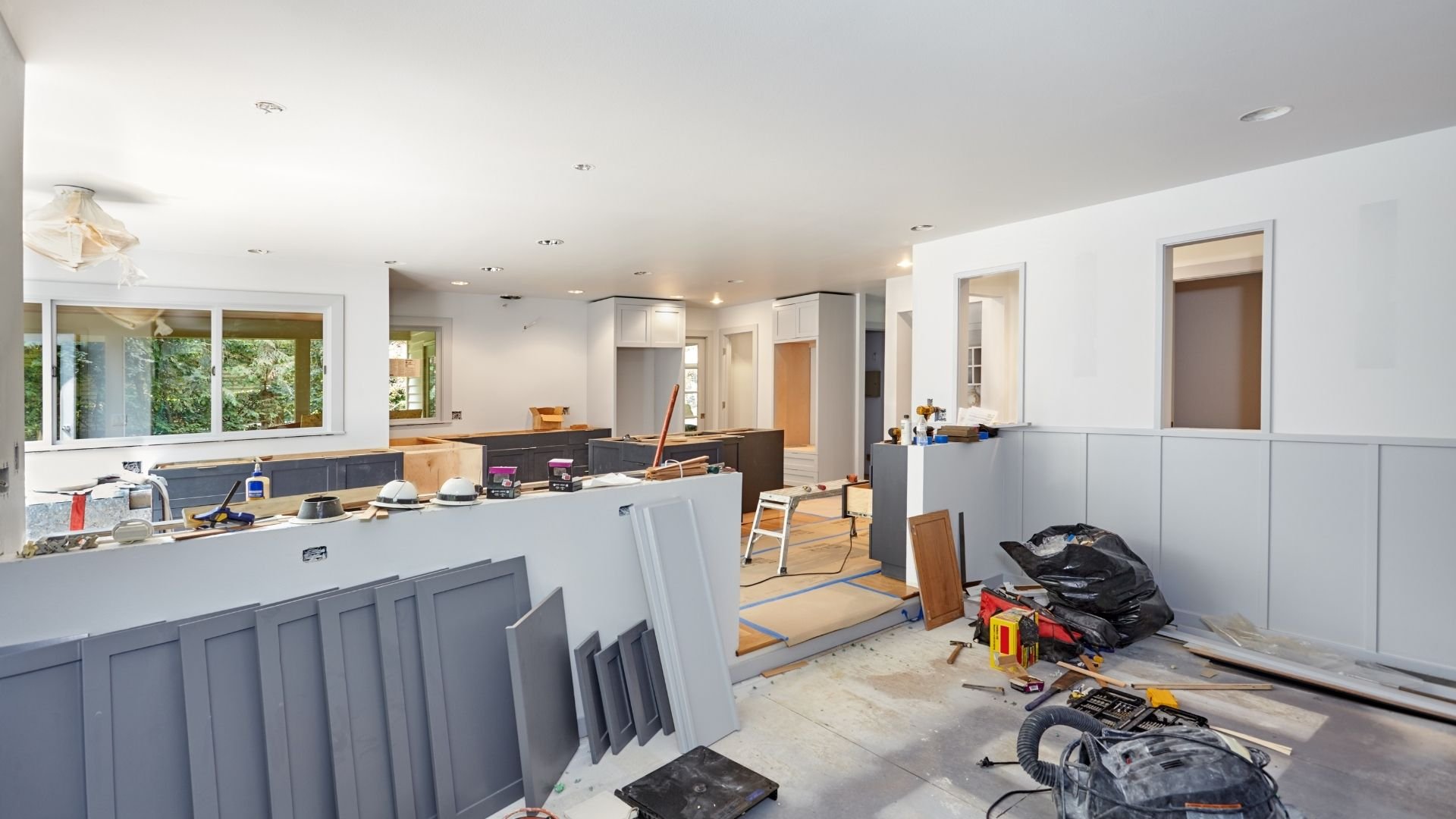 Modern kitchen under renovation with white cabinets, tools, and construction materials scattered throughout