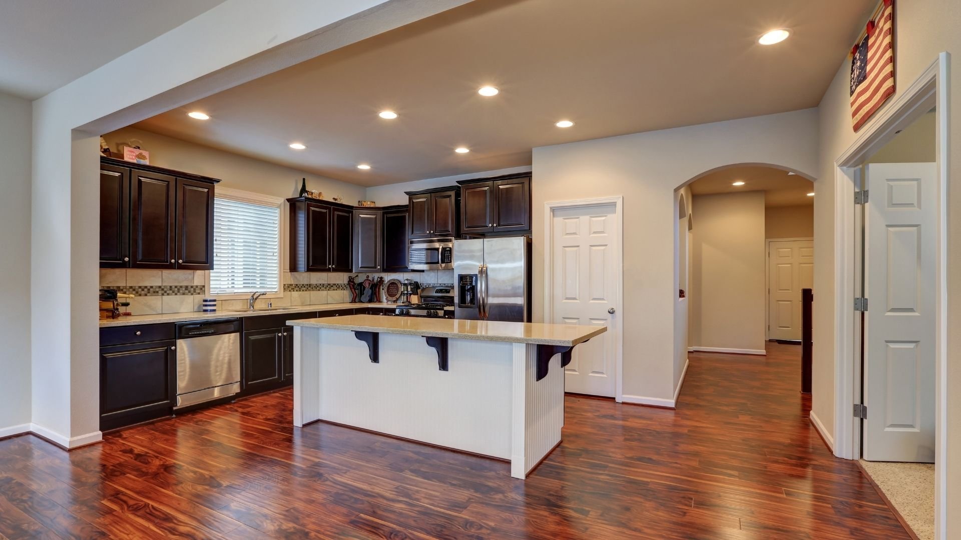 Modern kitchen with dark cabinetry, white island, stainless steel appliances, and hardwood flooring.
