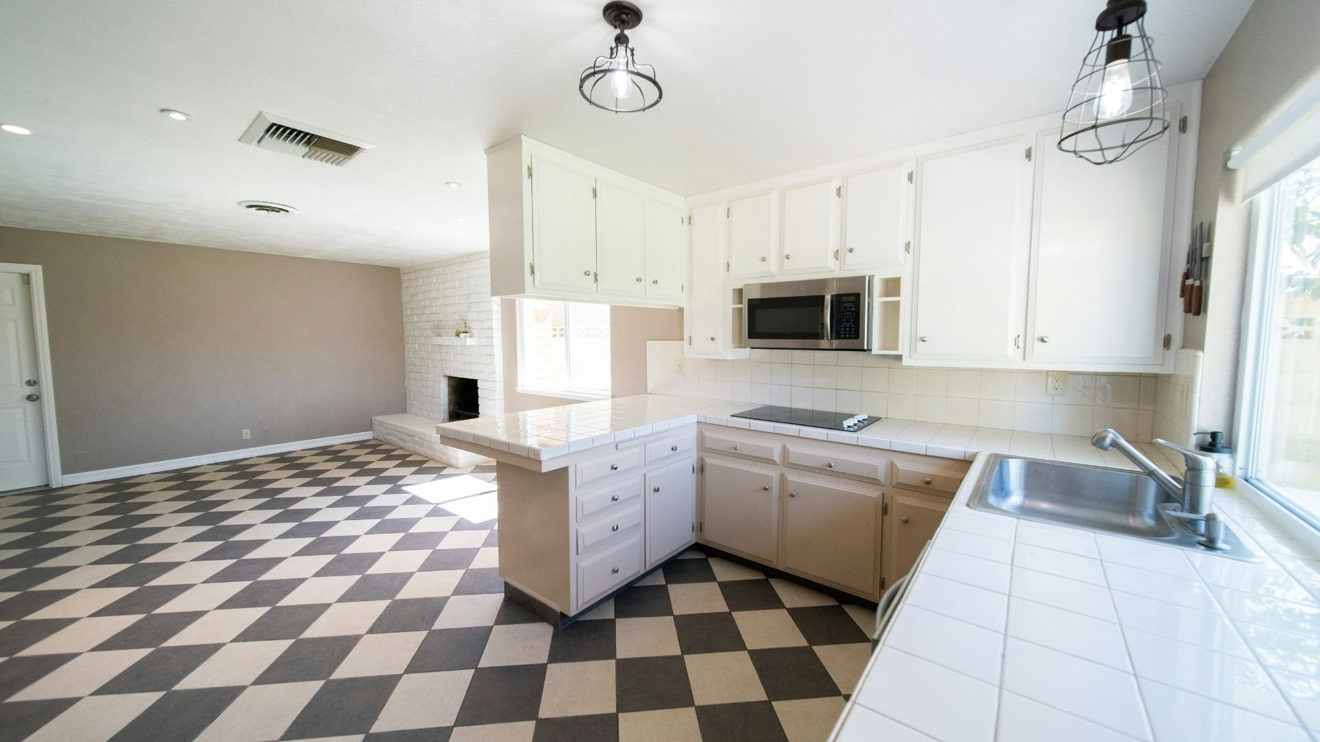 Spacious kitchen with white cabinets, diamond-patterned floor, and modern lighting fixtures.