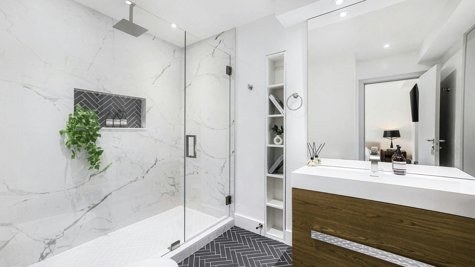 Modern bathroom with marble shower, white vanity, shelving, and herringbone floor tiles.