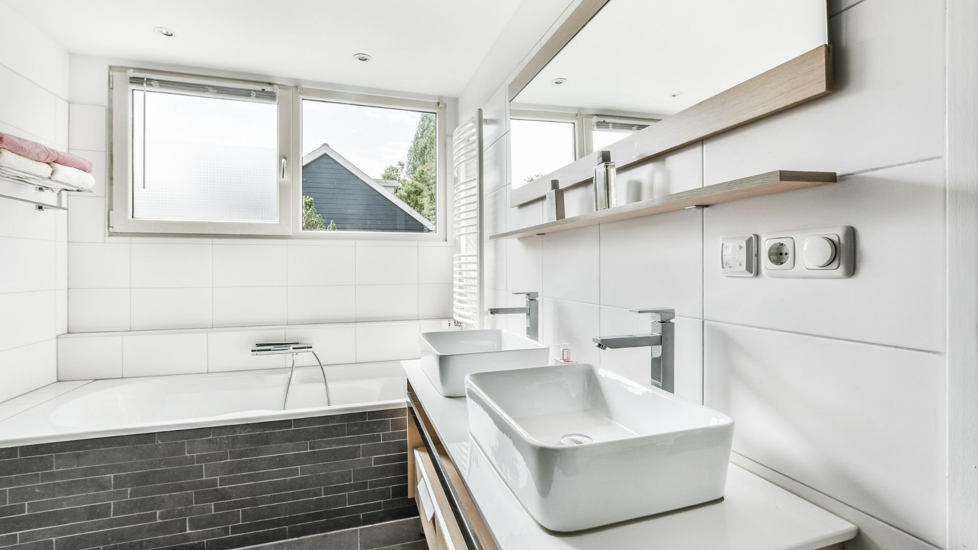 Modern bright bathroom with dual white sinks, tub, windows, and minimalist fixtures.
