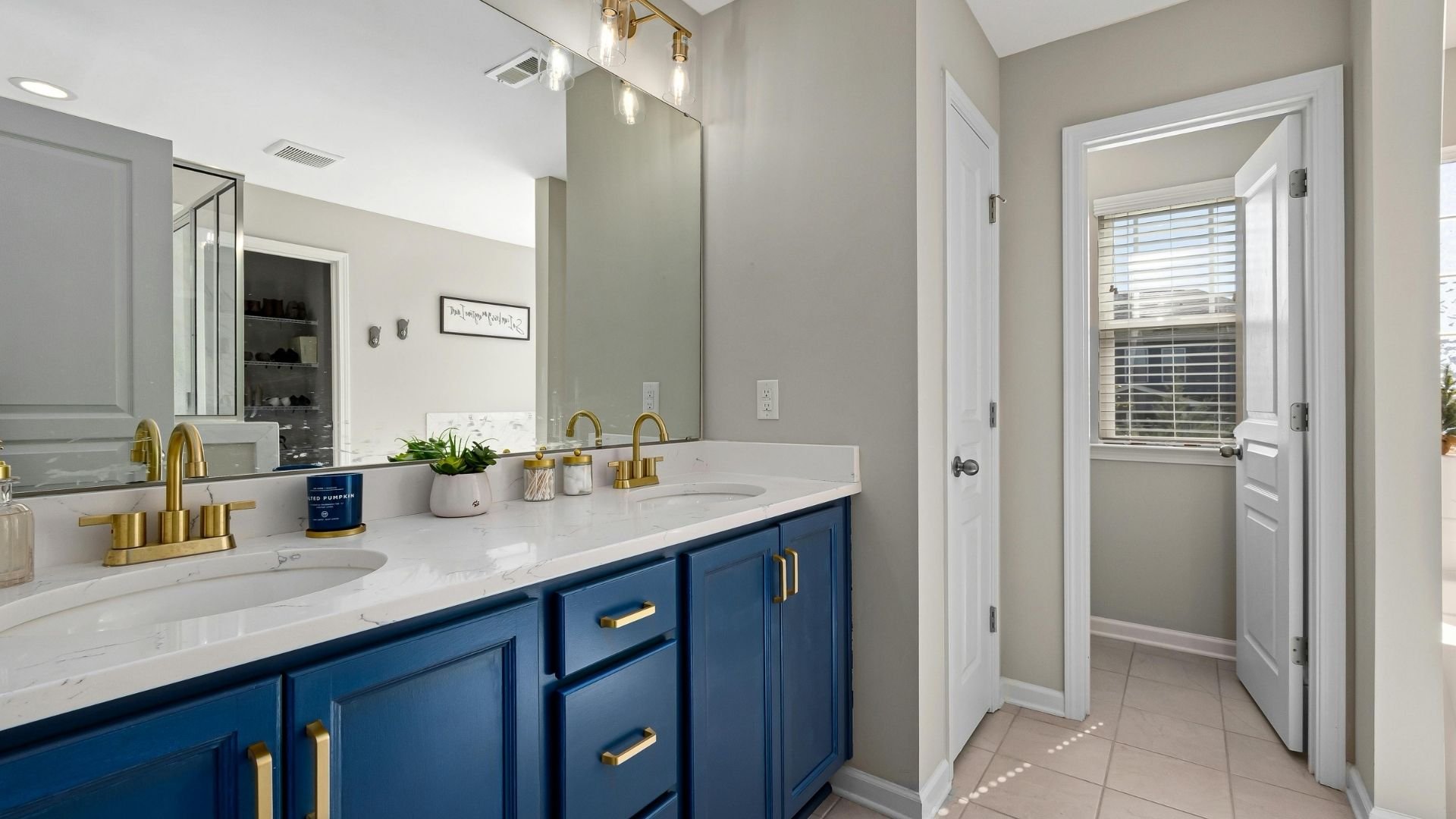 Modern bathroom with blue vanity, dual sinks, gold fixtures, white countertops, and tile flooring.