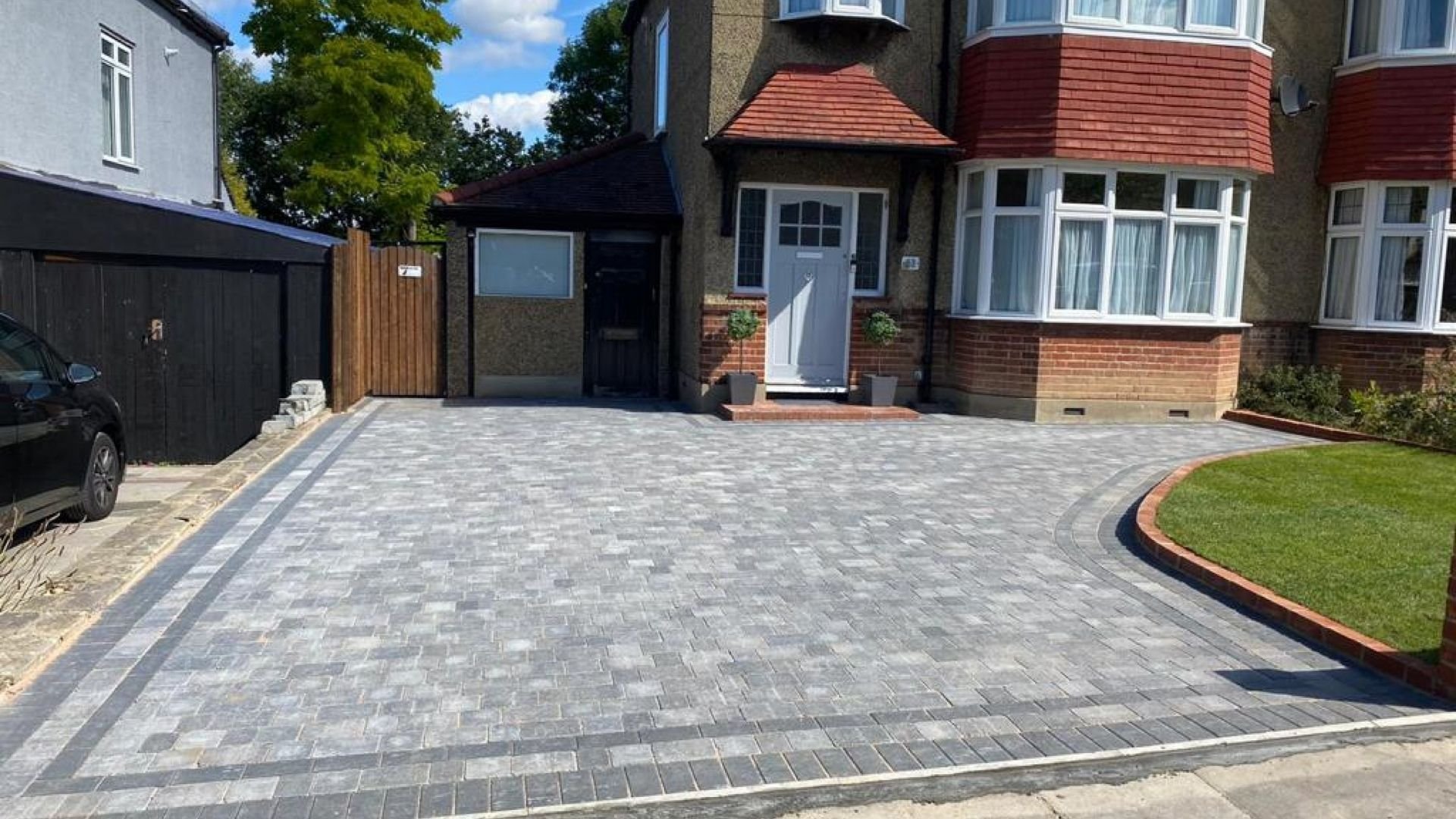Suburban brick houses with red-tiled roofs and a wide paved driveway with decorative border.