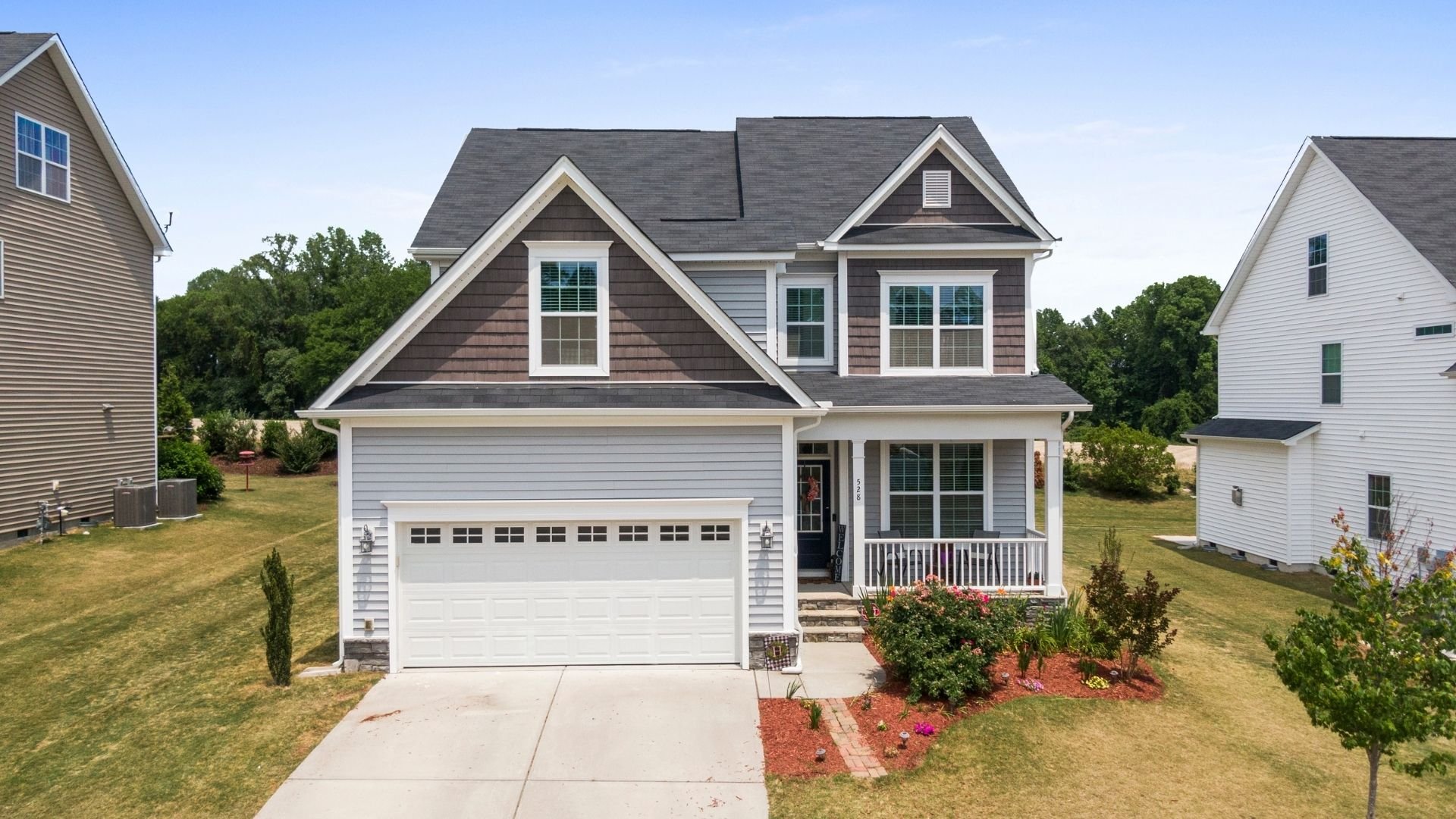 Modern two-story house with white garage, front porch, and landscaping in suburban neighborhood