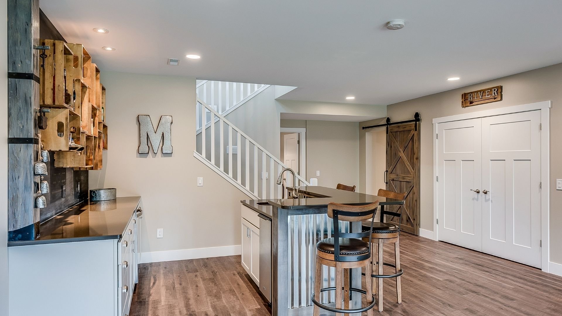 Modern rustic basement with kitchen, bar seating, staircase, and wooden accents throughout.